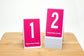 Tent style restaurant table numbers feature a bold white number on a bright pink background. Please place visibly is printed on the bottom of each number. Table numbers are printed on both sides perfect for high volume restaurants.